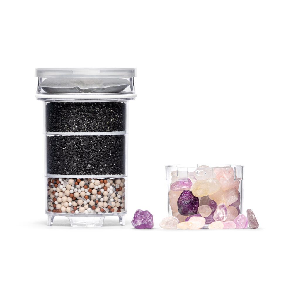 Mehrstufige Wasserfilter-Kartusche mit eingelegtem Kalkfilterpad, daneben ein separates Fach gefüllt mit bunten Edelsteinen zur Wasserveredelung.