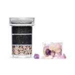 Mehrstufige Wasserfilter-Kartusche mit eingelegtem Kalkfilterpad, daneben ein separates Fach gefüllt mit bunten Edelsteinen zur Wasserveredelung.