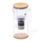 Eine Wasserfilter-Karaffe aus Glas mit einem Deckel aus hellem Holz und einem sichtbaren mehrschichtigen Filter im Inneren.