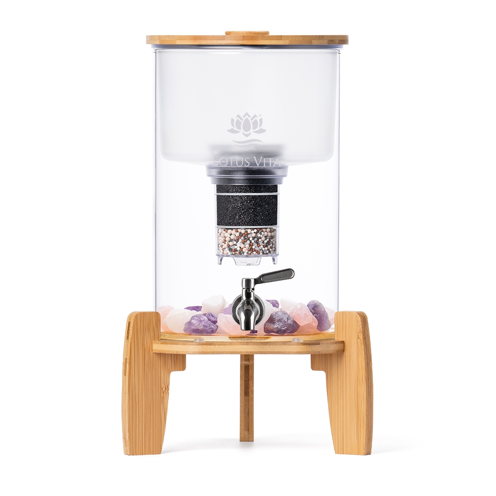 Ein Stand-Wasserfilter aus Glas mit einem Sockel und Deckel aus Bambus, einem Edelstahl-Zapfhahn und Edelsteinen im Behälter.
