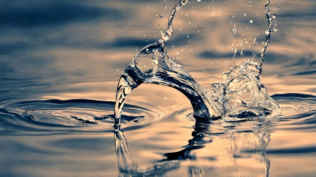 Klares, reines Wasser formt einen dynamischen Bogen über einer ruhigen Wasseroberfläche in warmem Abendlicht.