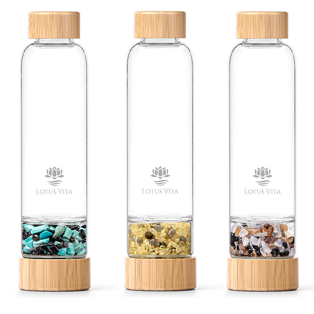 Drei Glasflaschen mit Bambusdeckeln und separaten Kammern, gefüllt mit verschiedenen Edelsteinmischungen, nebeneinander aufgereiht.