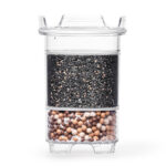 Eine transparente Wasserfilter-Kartusche, die im oberen Bereich mit Aktivkohle und im unteren Bereich mit Mineralkugeln gefüllt ist.